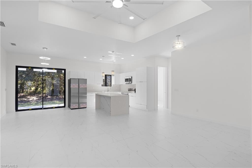 Kitchen with white cabinets, a tray ceiling, open floor plan, stainless steel appliances, and recessed lighting