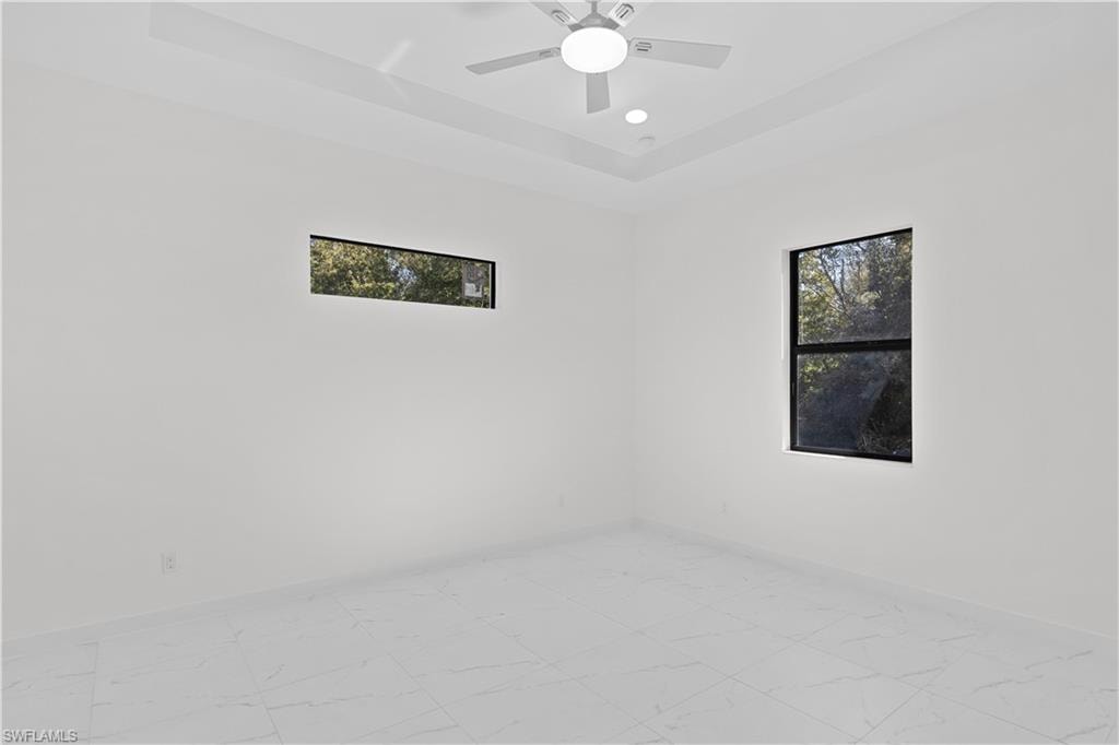 Empty room featuring plenty of natural light, a raised ceiling, light marble finish floors, and recessed lighting