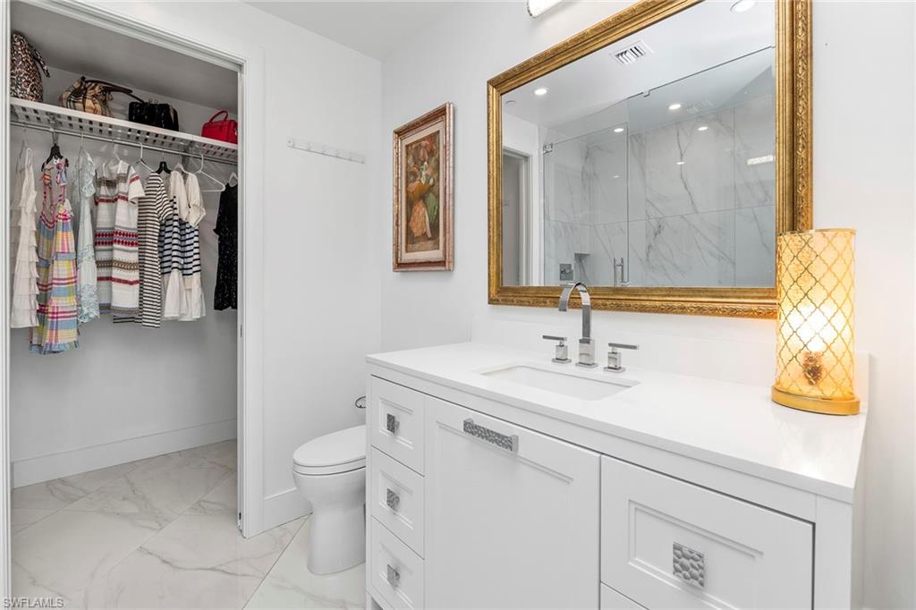 Full bath featuring light marble finish flooring, a marble finish shower, vanity, abd a walk in closet.