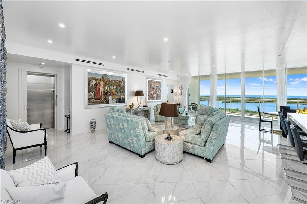Living room featuring a water view, elevator, floor to ceiling windows, and light marble finish flooring