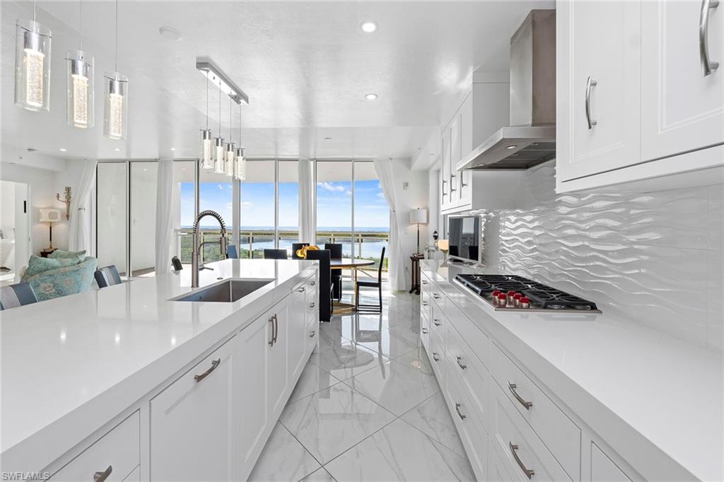 Kitchen featuring white cabinetry, pendant lighting, wall chimney range hood, backsplash, and expansive windows