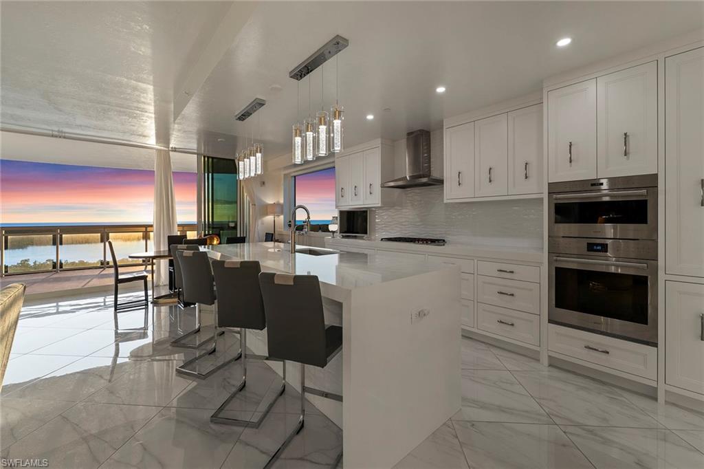 Kitchen featuring white cabinets, a breakfast bar, stainless steel double oven, hanging light fixtures, and light stone countertops