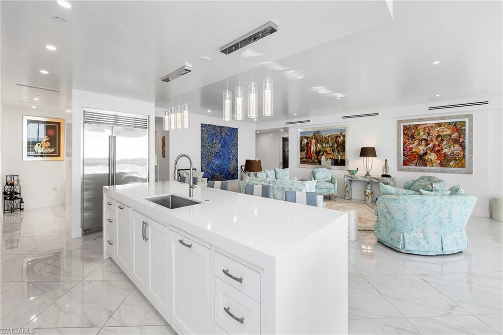 Kitchen with white cabinetry, stainless steel built in refrigerator, open floor plan, pendant lighting, and light stone countertops