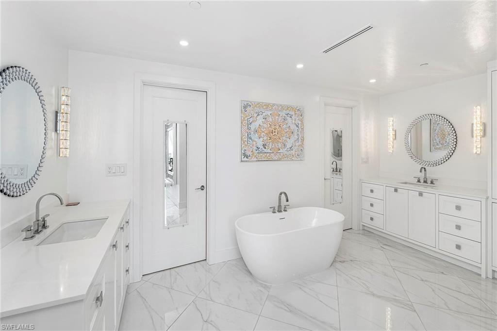 Full bath featuring two vanities, a freestanding tub, light marble finish floors, and recessed lighting