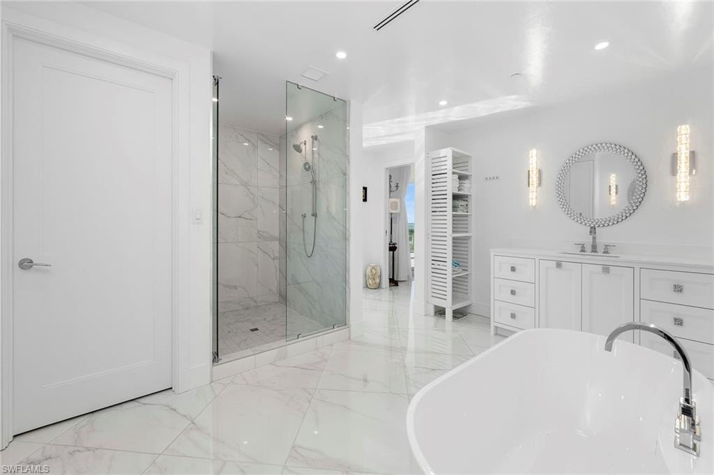 Full bath featuring vanity, a freestanding tub, a marble finish shower, recessed lighting, and light marble finish floors
