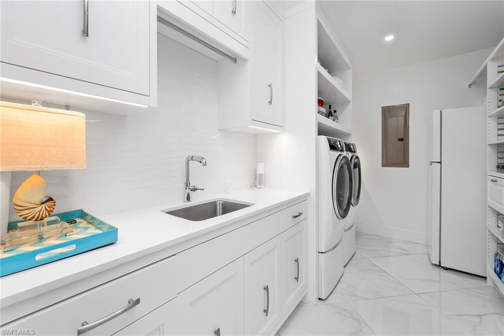 Washroom featuring washer and clothes dryer, electric panel, light marble finish flooring, recessed lighting, and cabinet space