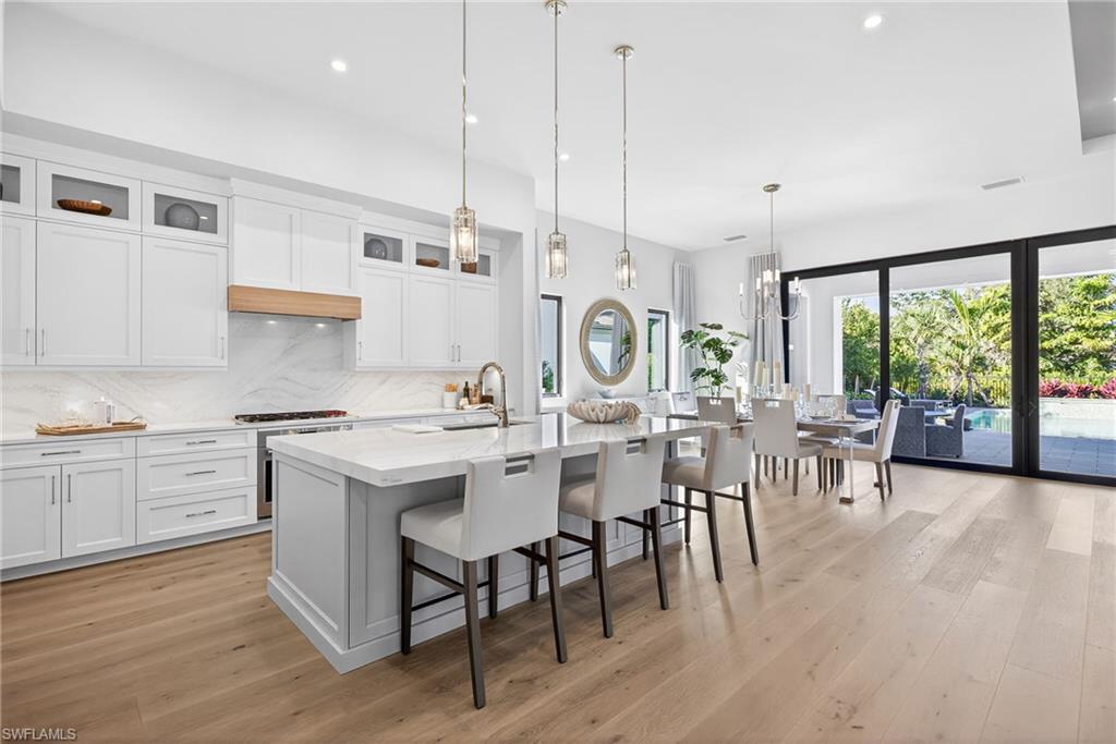 Kitchen with glass insert cabinets, white custom cabinets, elegant and simple hanging light fixtures, large kitchen breakfast bar