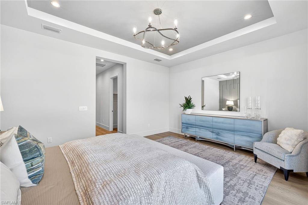 Coastal contemporary master suites' space is bright and airy featuring a tray ceiling, pretty chandelier and recessed lighting
