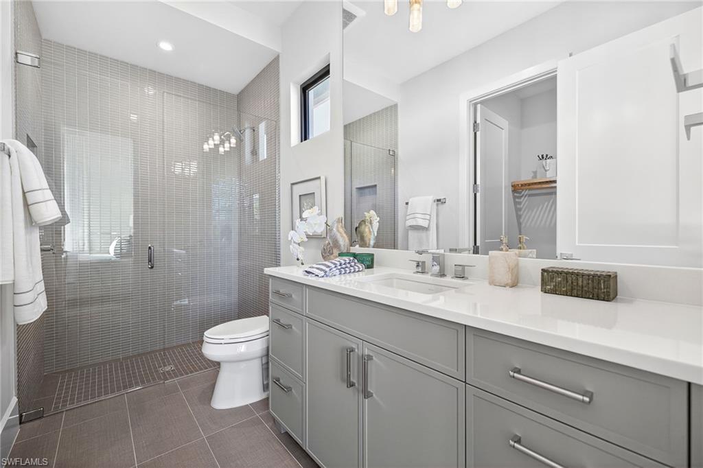 Guest bathroom 1 with a large tiled shower stall, large vanity, and dark tile patterned floors