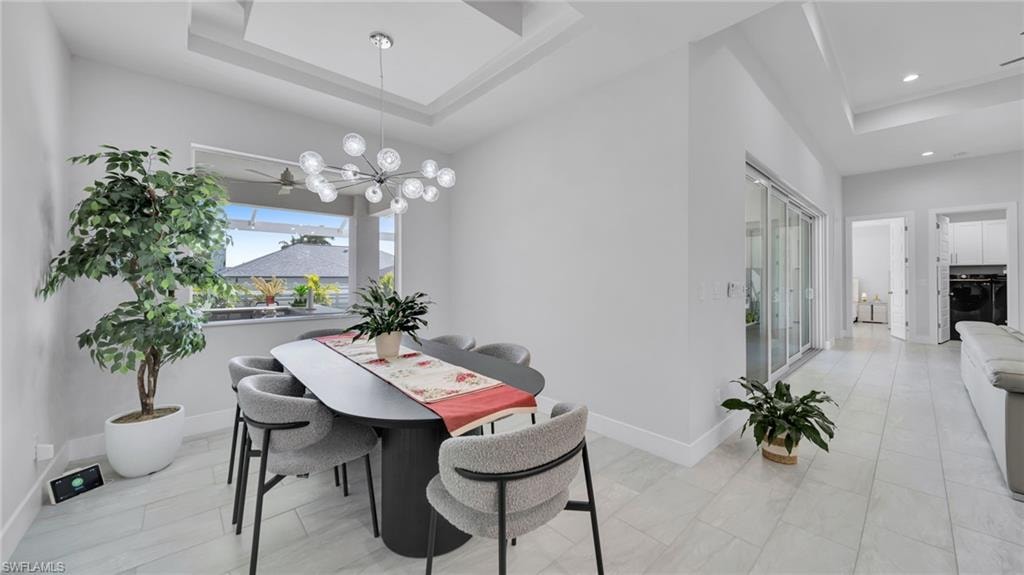 Dining space featuring a tray ceiling, a chandelier, washer / clothes dryer, and recessed lighting