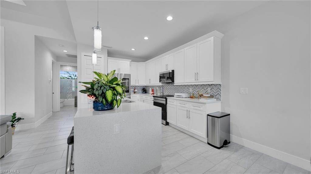 Kitchen featuring light stone counters, white cabinetry, appliances with stainless steel finishes, pendant lighting, and an island with sink