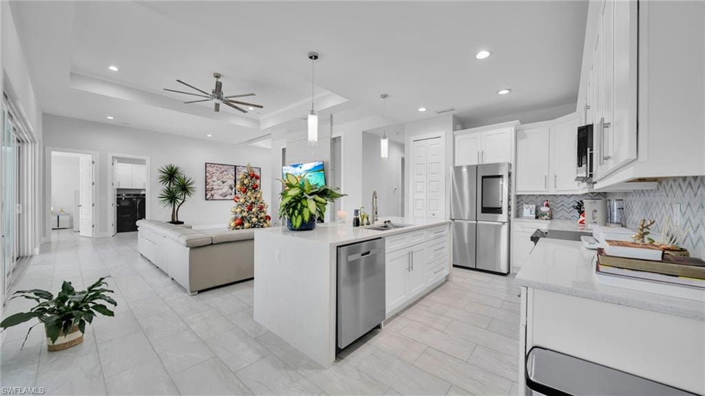 Kitchen with open floor plan, appliances with stainless steel finishes, a tray ceiling, white cabinetry, and recessed lighting