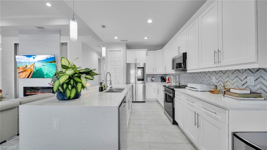 Kitchen featuring pendant lighting, stainless steel appliances, light stone counters, recessed lighting, and white cabinetry