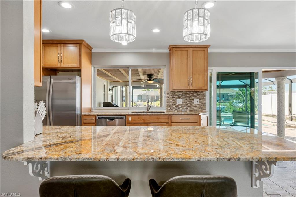 Kitchen featuring a kitchen breakfast bar, light stone counters, appliances with stainless steel finishes, crown molding, and tasteful backsplash