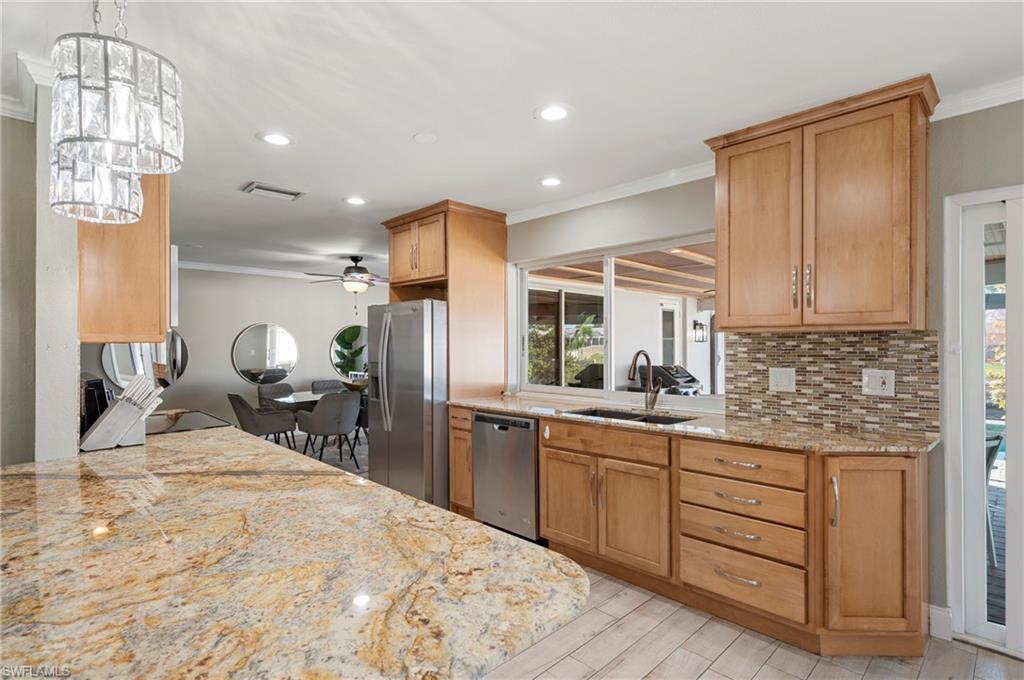 Kitchen featuring light stone counters, ornamental molding, appliances with stainless steel finishes, brown cabinetry, and recessed lighting