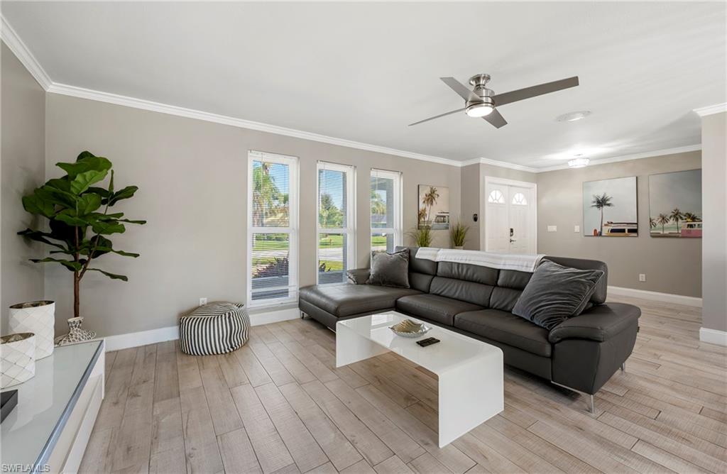 Living room with ornamental molding, light wood-style flooring, and a ceiling fan