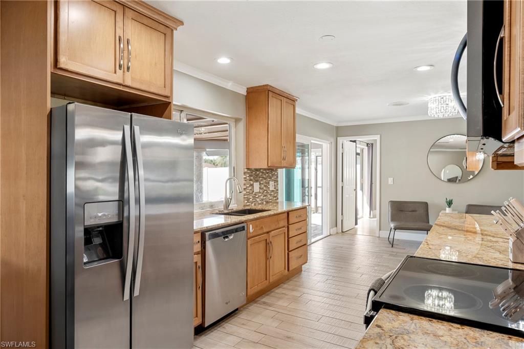 Kitchen featuring appliances with stainless steel finishes, light stone countertops, crown molding, light wood-style floors, and recessed lighting