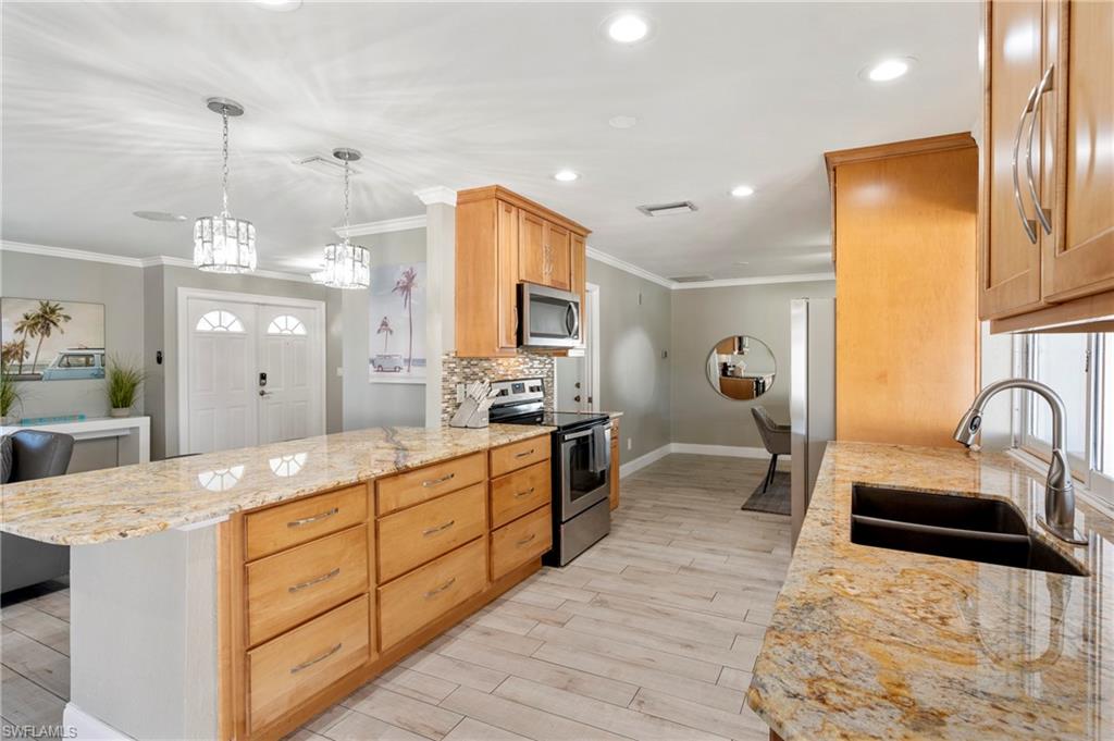 Kitchen featuring light stone countertops, stainless steel appliances, pendant lighting, crown molding, and decorative backsplash