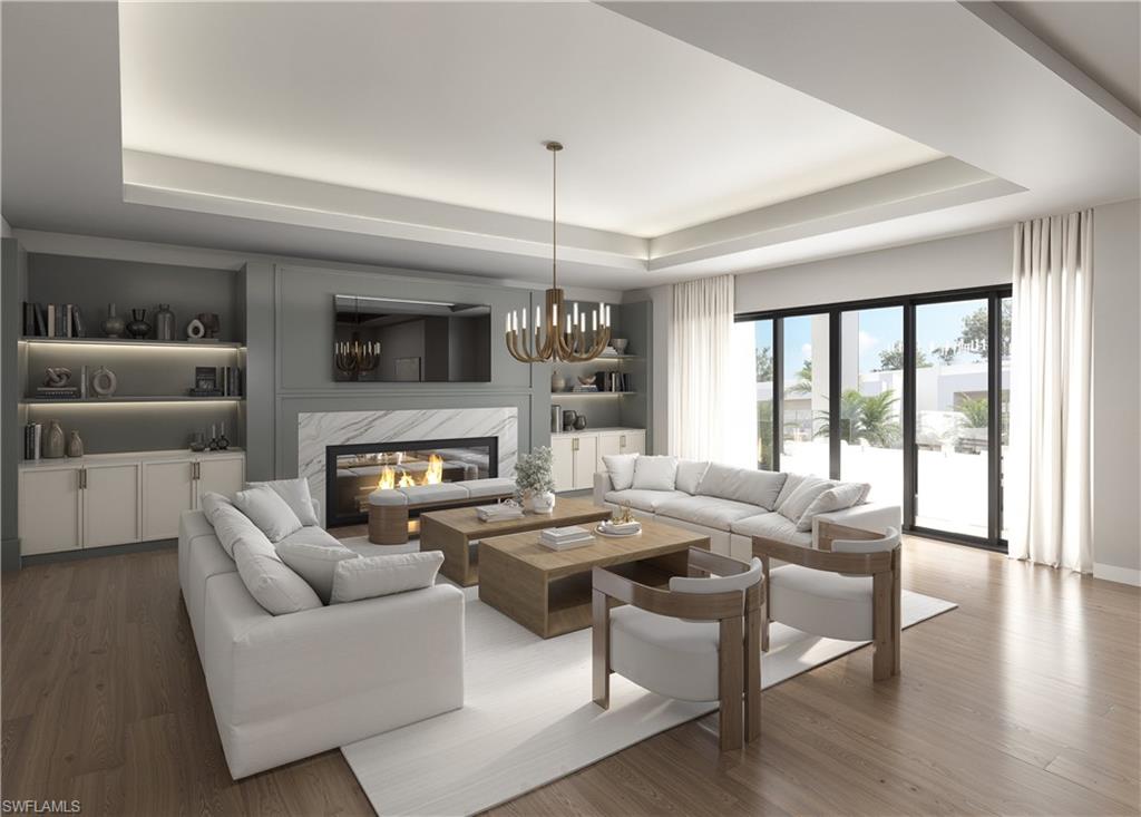 Living room with a premium fireplace, wood finished floors, a chandelier, a tray ceiling, and built in shelves