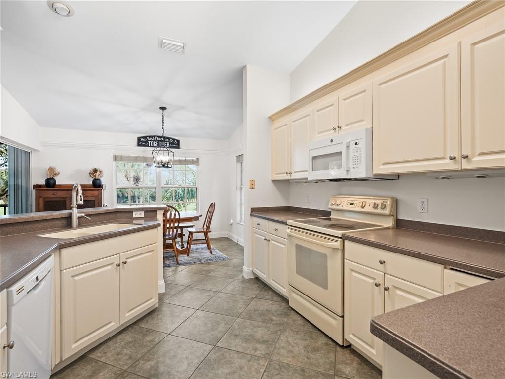 Kitchen with white appliances, dark countertops, a chandelier, and dark tile patterned flooring
