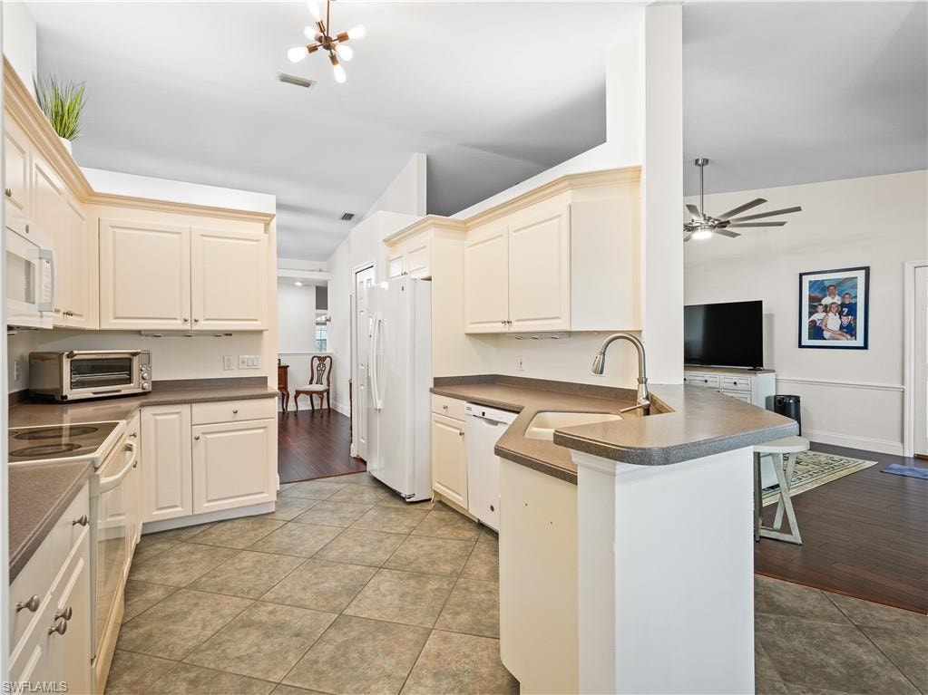 Kitchen with dark countertops, white appliances, a peninsula, a kitchen breakfast bar, and a ceiling fan