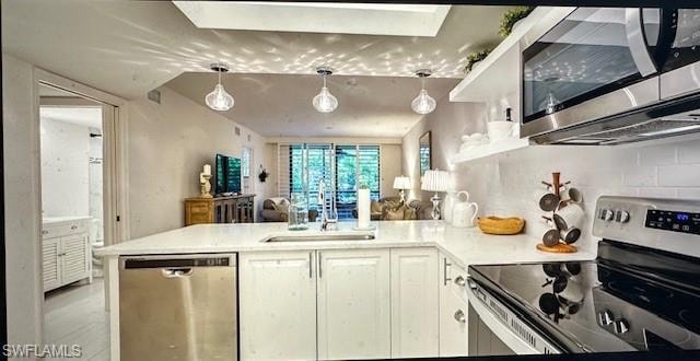 Kitchen with stainless steel appliances, a peninsula, white cabinets, and hanging light fixtures