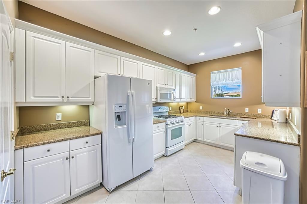Kitchen with light stone counters, white cabinetry, white appliances, recessed lighting, and light tile patterned floors