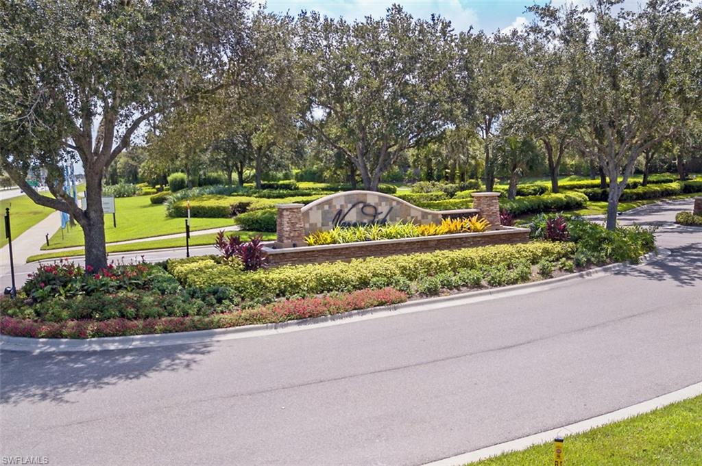 Community sign featuring a lawn and view of scattered trees