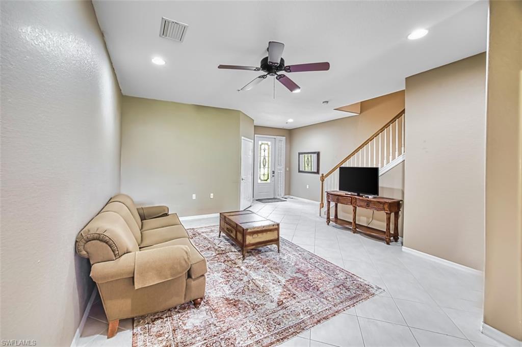 Living room featuring light tile patterned flooring, recessed lighting, ceiling fan, and stairs
