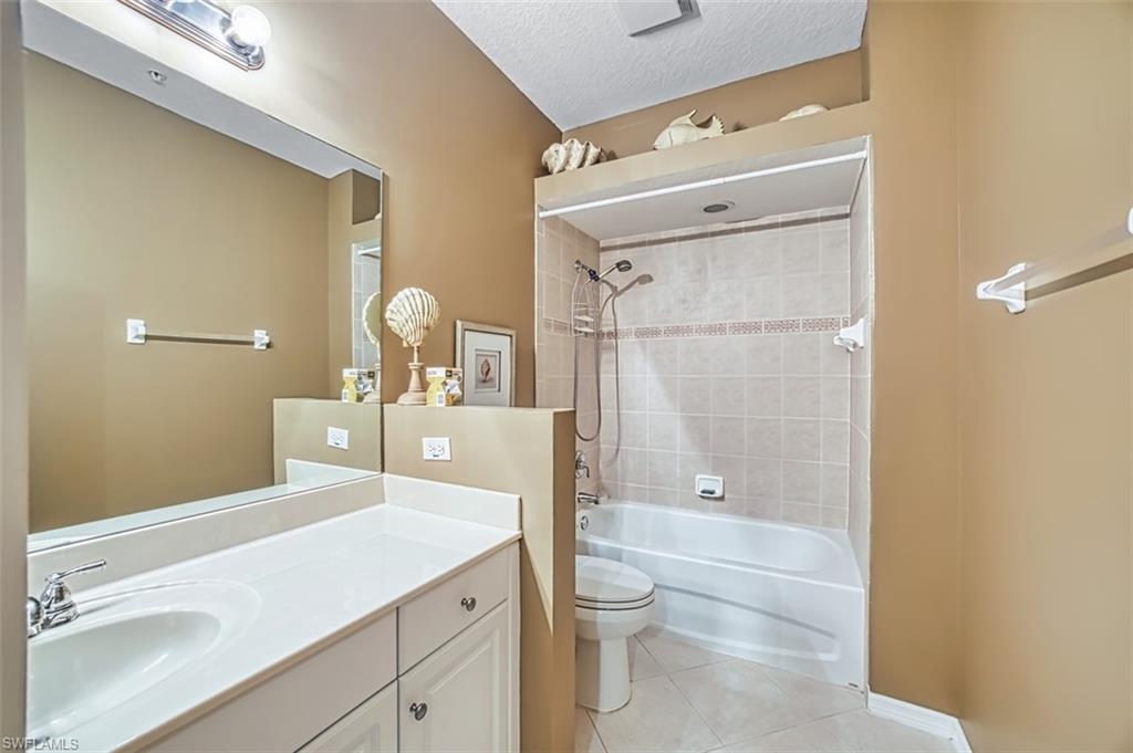 Full bath with vanity, light tile patterned flooring, washtub / shower combination, and a textured ceiling