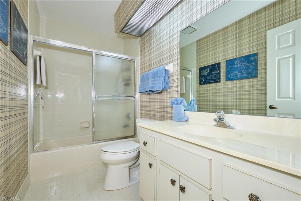 Full bath with vanity, light tile patterned flooring, combined bath / shower with glass door, and tile walls