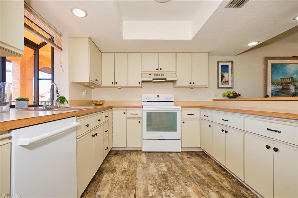 Kitchen featuring white appliances, light countertops, cream cabinets, a tray ceiling, and light wood-style flooring