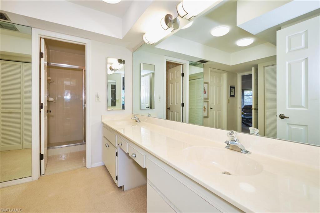Bathroom featuring a closet, double vanity, a shower stall, and light carpet