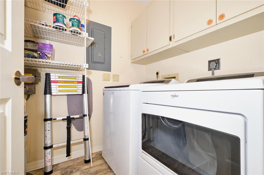 Laundry area with cabinet space, electric panel, washer and dryer, and light wood-style flooring