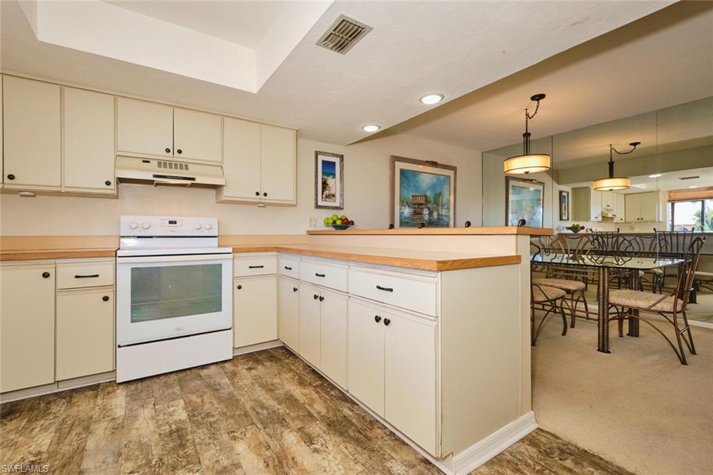 Kitchen with electric stove, a peninsula, light countertops, hanging light fixtures, and under cabinet range hood