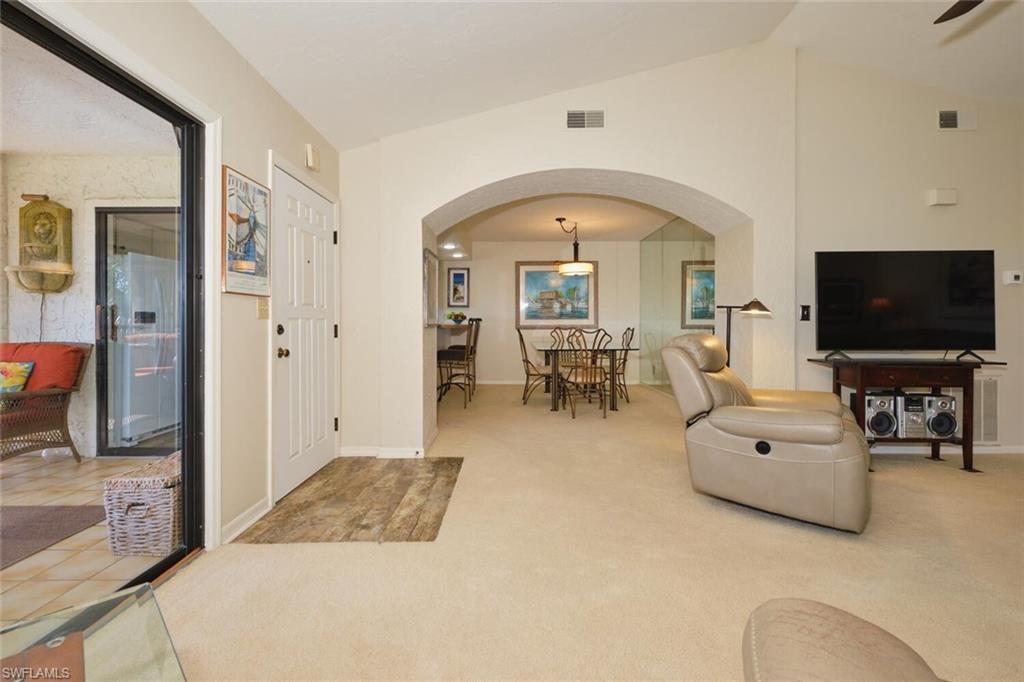 Living room featuring arched walkways, carpet, and vaulted ceiling