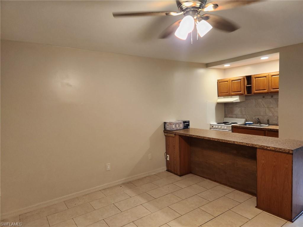 Kitchen featuring dark countertops, a peninsula, decorative backsplash, white electric range oven, and ceiling fan