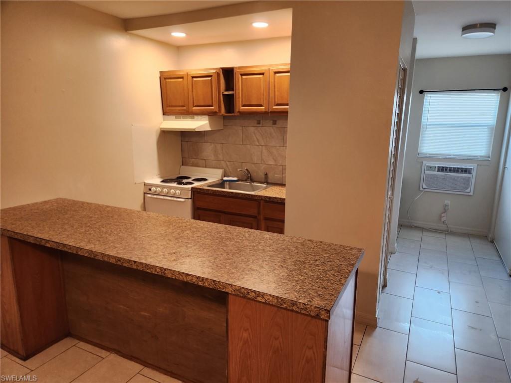Kitchen featuring decorative backsplash, a peninsula, electric stove, brown cabinets, and under cabinet range hood