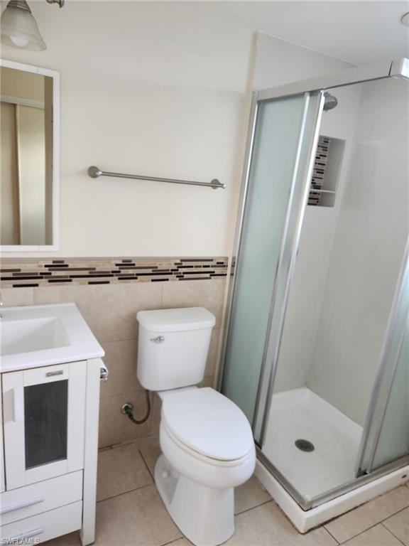 Full bathroom featuring a shower stall, vanity, light tile patterned floors, tile walls, and wainscoting