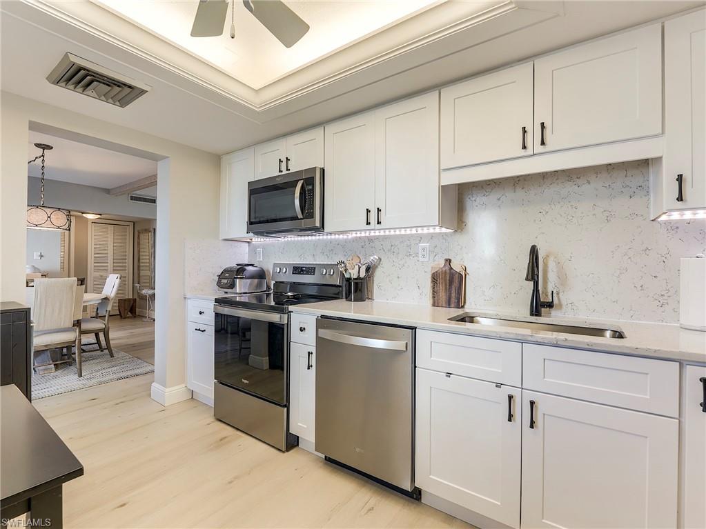 Kitchen with appliances with stainless steel finishes, white cabinets, light stone counters, light wood-style flooring, and tasteful backsplash
