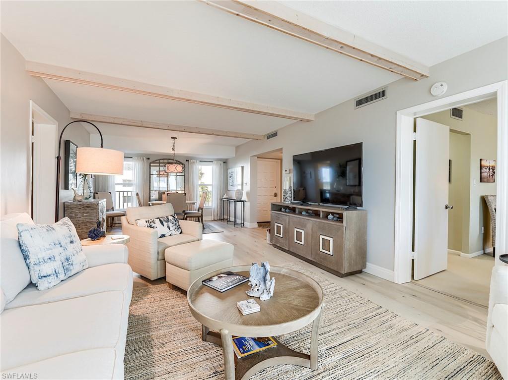 Living room featuring beamed ceiling, light wood-style flooring, and a chandelier