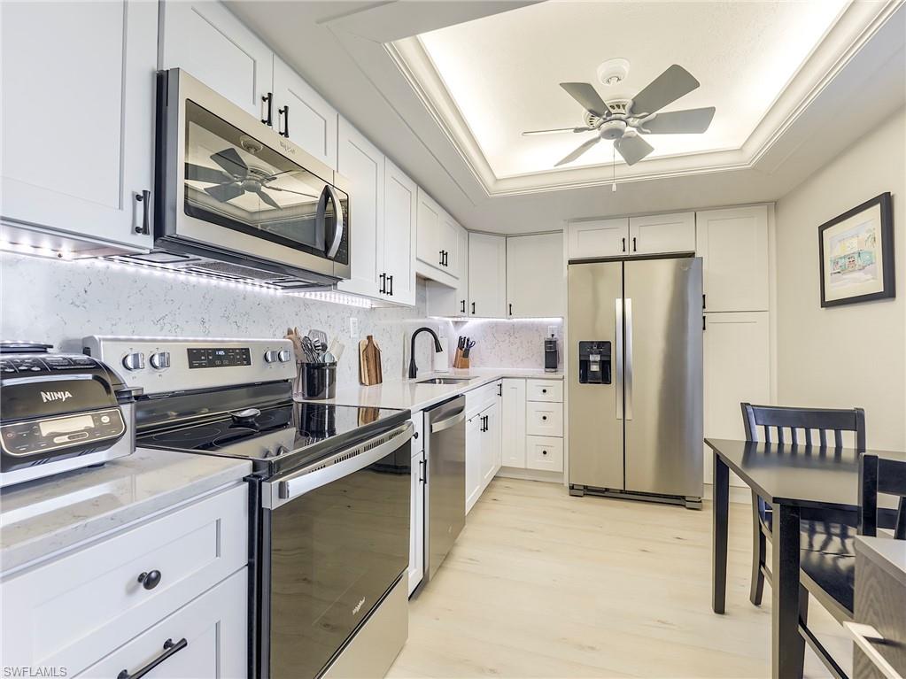 Kitchen featuring stainless steel appliances, a ceiling fan, white cabinetry, a raised ceiling, and light stone countertops