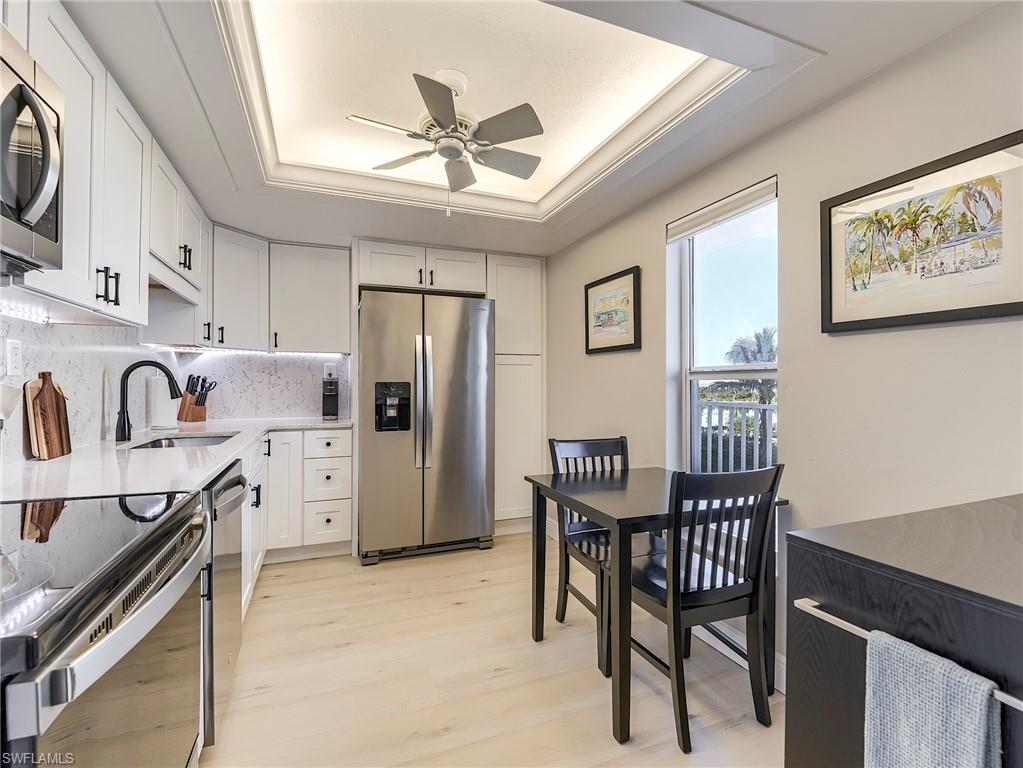 Kitchen featuring appliances with stainless steel finishes, a raised ceiling, light stone countertops, white cabinets, and light wood-type flooring