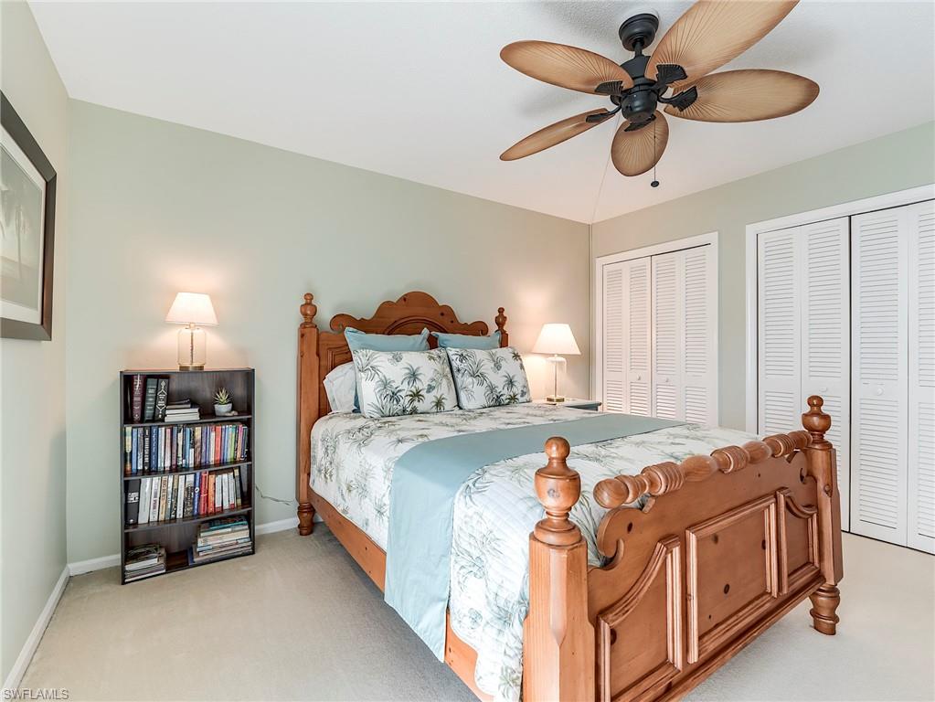 Bedroom with two closets, light colored carpet, and a ceiling fan