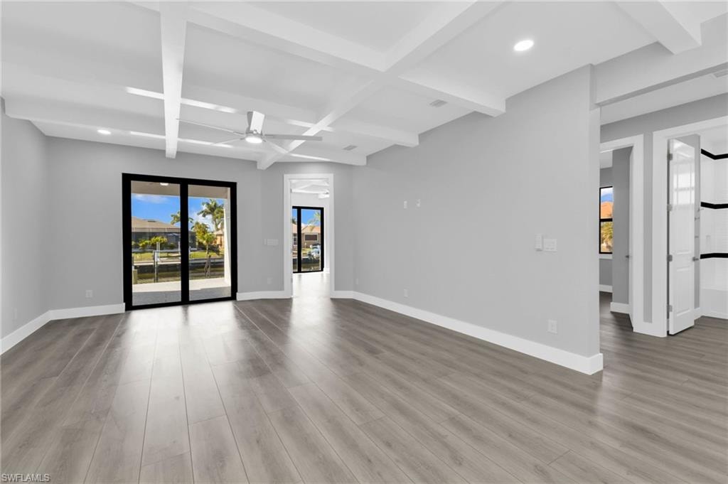 Spare room featuring beamed ceiling, healthy amount of natural light, ceiling fan, coffered ceiling, and light wood-type flooring