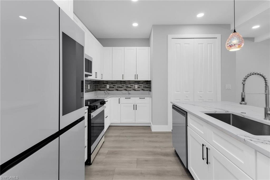 Kitchen featuring appliances with stainless steel finishes, light stone counters, hanging light fixtures, white cabinets, and tasteful backsplash