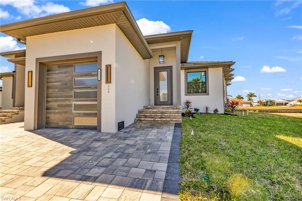 Entrance to property with stucco siding, a lawn, and an attached garage