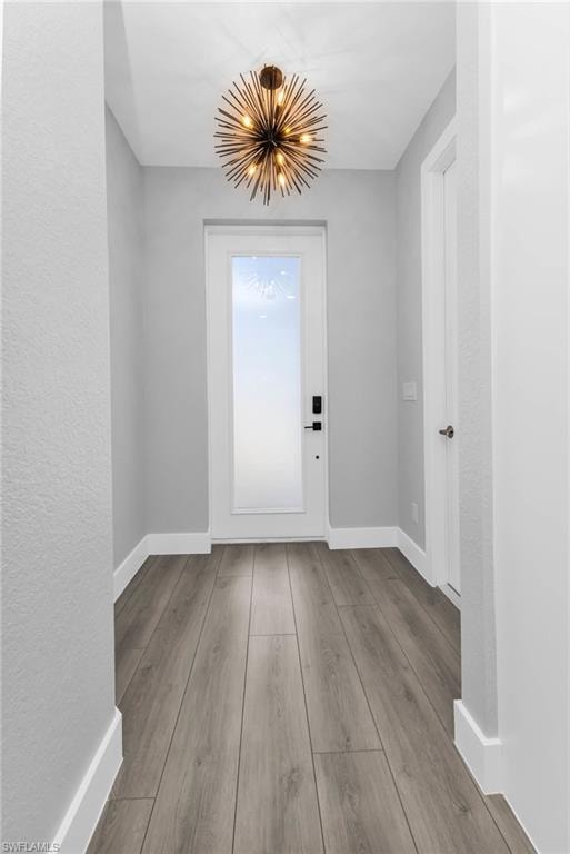 Doorway featuring a chandelier, wood finished floors, and a textured wall
