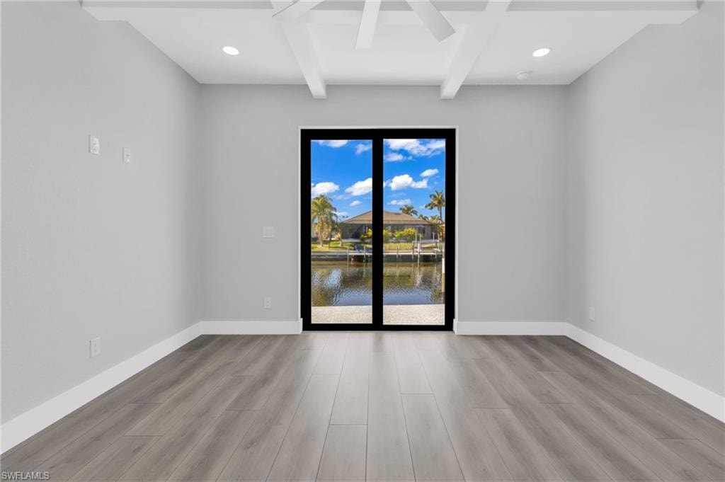 Spare room with beam ceiling, a water view, light wood finished floors, recessed lighting, and coffered ceiling