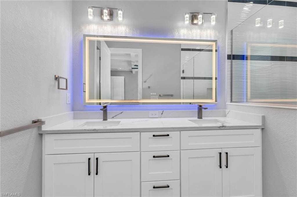 Full bathroom with a textured wall, double vanity, and an enclosed shower